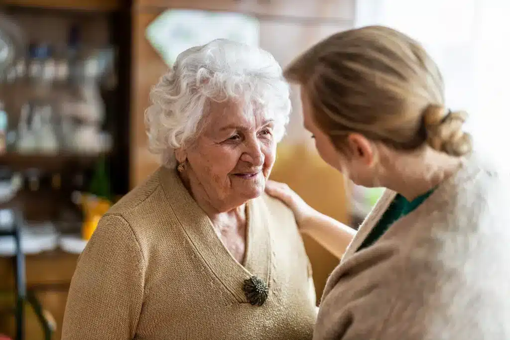 Caregiver speaking warmly with an older adult during a supportive assisted living interaction.