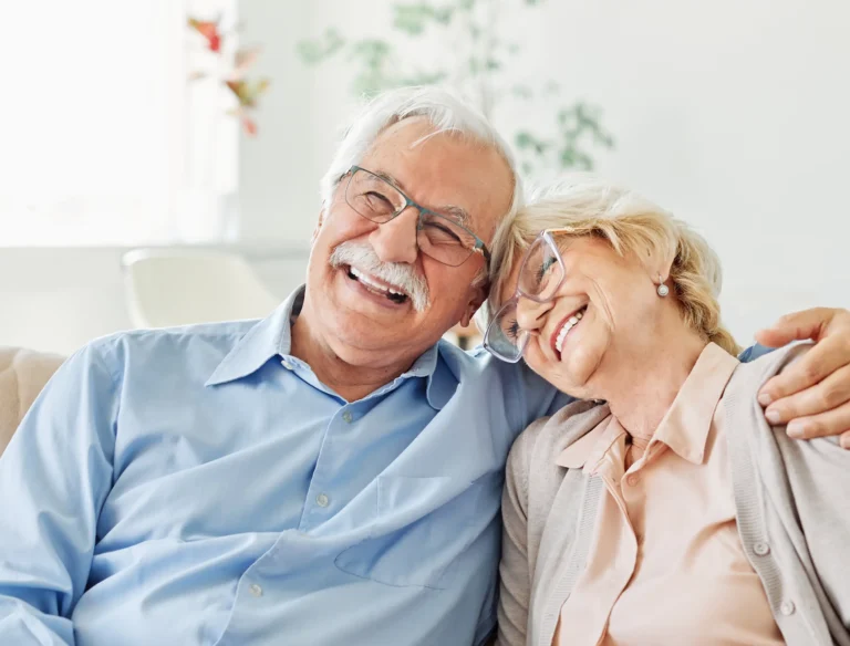 Two Mirror Lake Assisted Living residents smiling and embracing while sitting indoors.